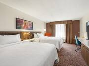 Spacious guestroom featuring two comfortable queen beds, TV, and work desk.