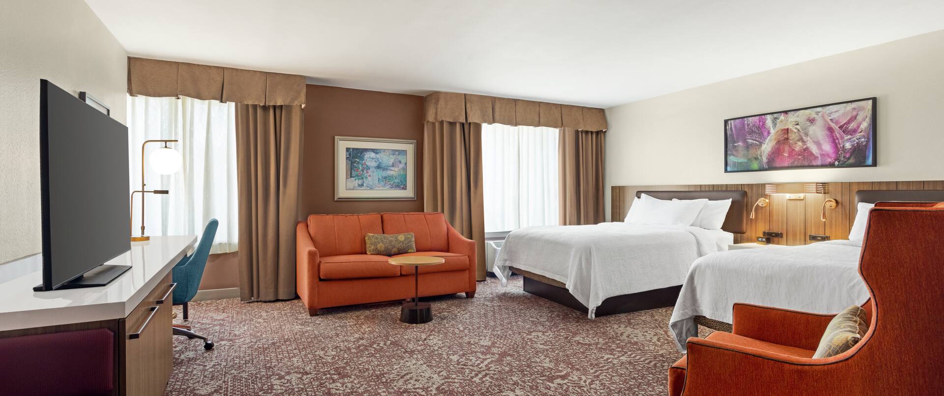 Spacious guestroom featuring two comfortable queen beds, sofa, work desk, and TV.