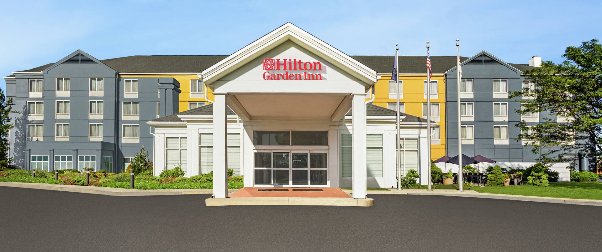 Welcoming Hilton Garden Inn hotel exterior featuring eye-catching design, lush landscaping, and blue sky.