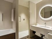 Suite Bathroom with Tub and Separate Shower and View of Vanity Area with Round Lit Mirror