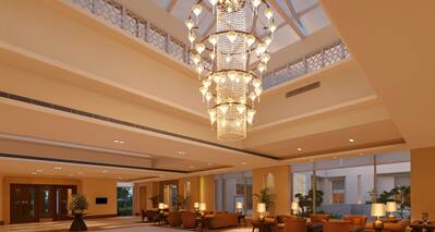 Lobby With Illuminated Chandelier, and Lounge Area With Armchairs, Tables, and Illuminated Lamps