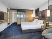 King Bed with Side Tables Facing TV, Glass Table, and Soft seating with a Harbor View