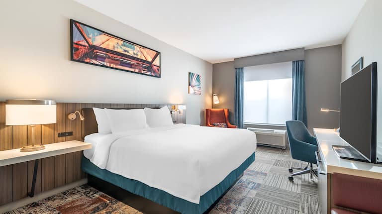 Hotel room with one king bed, a work desk and chair, then the wall-mounted TV.