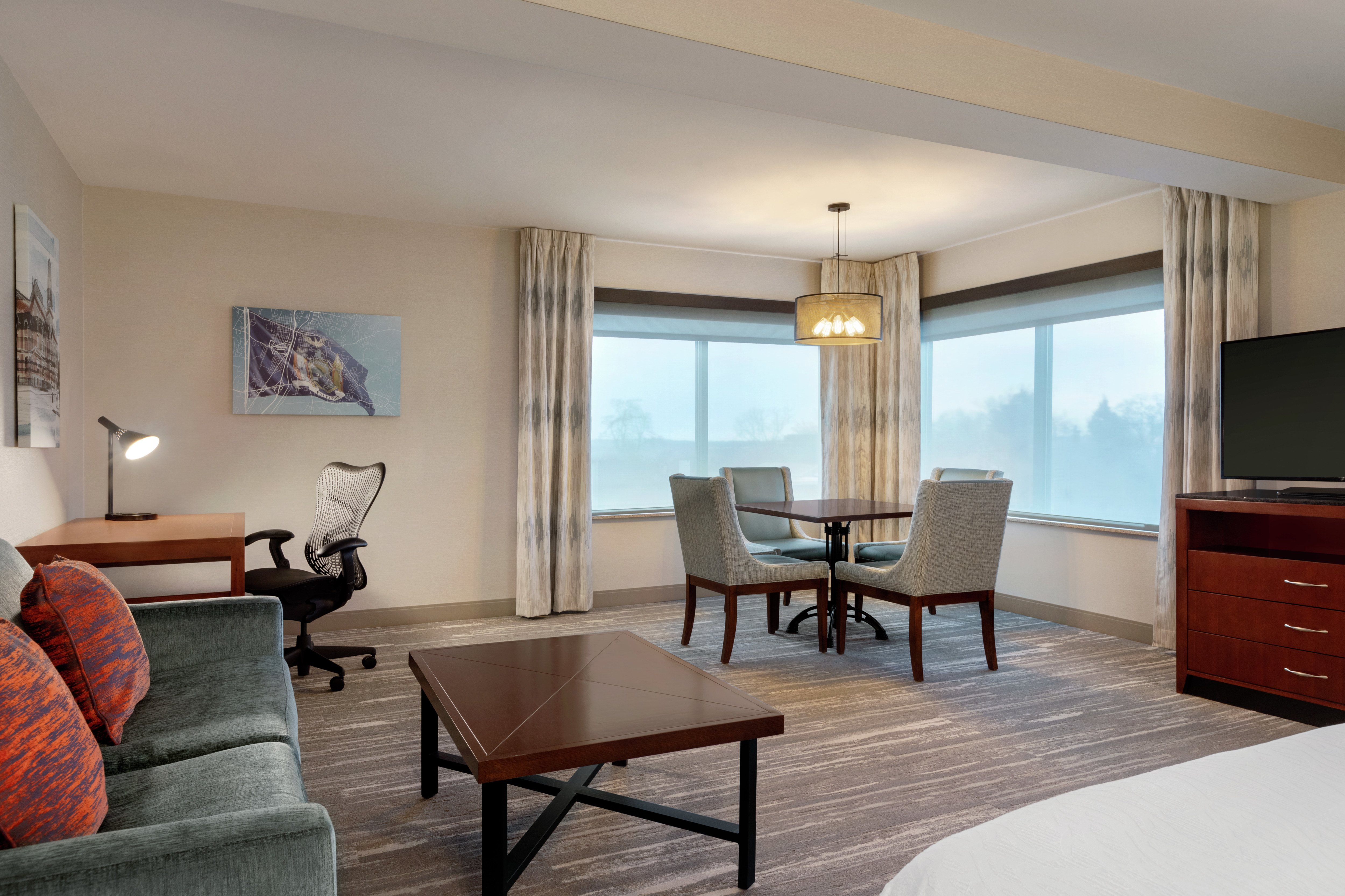 Spacious junior suite living area featuring large windows, dining table, sofa, TV, and work desk.