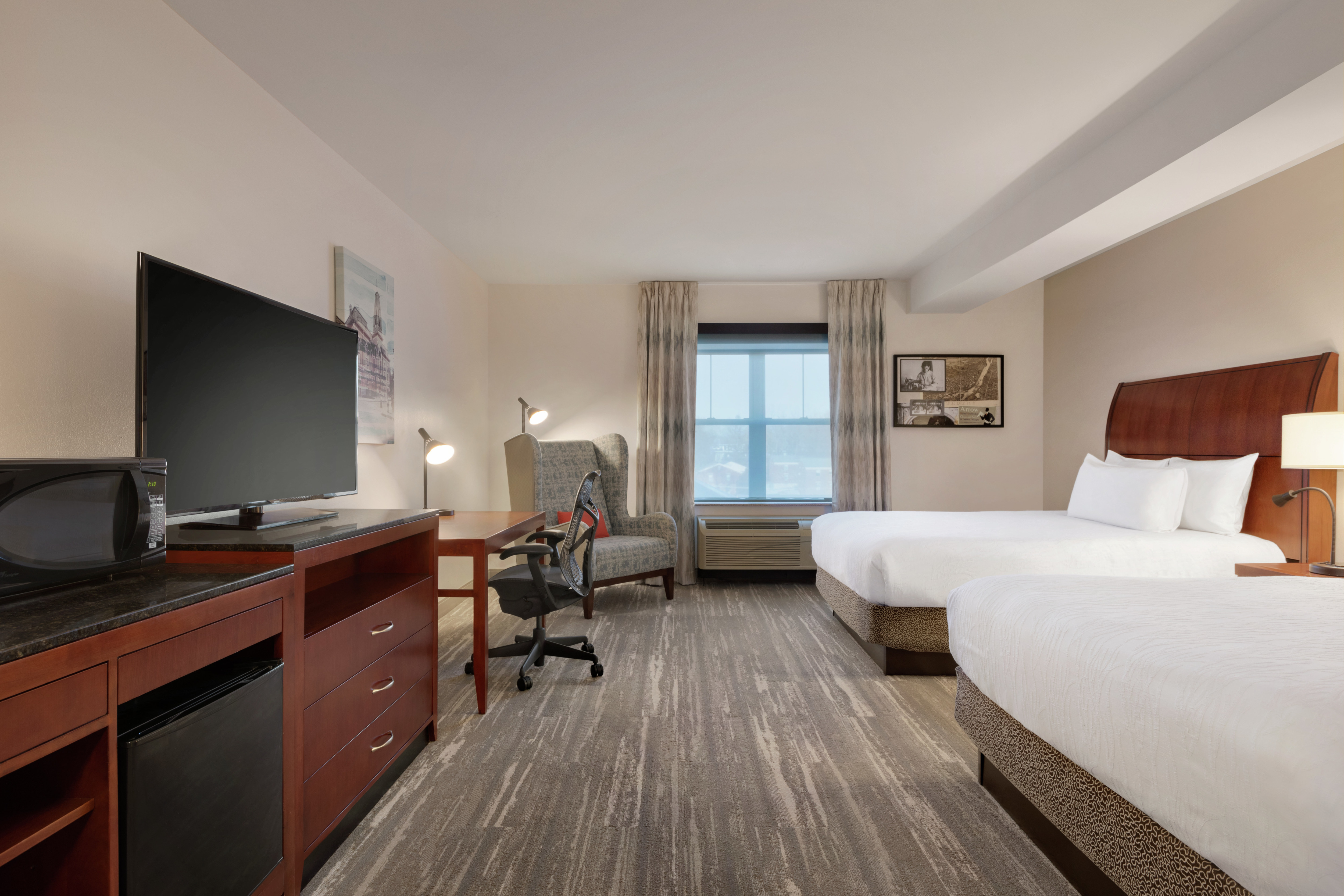 Spacious premium guestroom featuring convenient microwave and mini-fridge, TV, work desk, and two comfortable queen beds.
