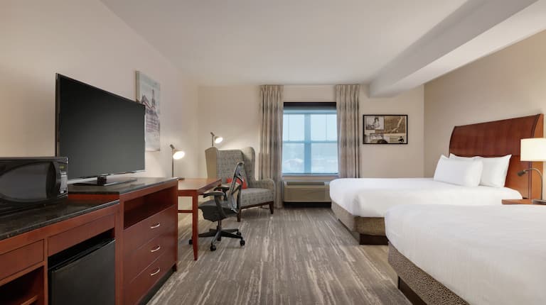 Spacious premium guestroom featuring convenient microwave and mini-fridge, TV, work desk, and two comfortable queen beds.