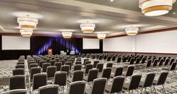 Spacious hotel ballroom featuring theater setup and stage with podium at front of room.