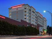 Modern Hilton Garden Inn hotel exterior featuring large event space, glowing guestroom windows, and dusk sky.