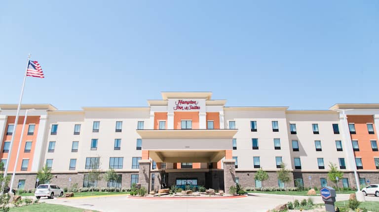 Daytime View of Hotel Exterior, Signage, Flagpole, Landscaping, Circle Drive, and Parking Lot