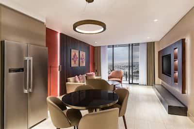 Joint kitchen and lounge area with round dining table, chairs, fridge, sofa, TV and balcony overlooking city