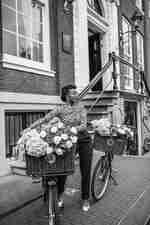 Mujer posando con una bicicleta y una canasta llena de flores