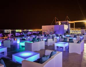 Diwan Rooftop Lounge Area With Tables and Seating Illuminated in Blue at Night
