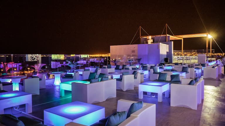 Diwan Rooftop Lounge Area With Tables and Seating Illuminated in Blue at Night