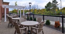 Daytime View of Hotel Patio With Tables, Chairs, Pavilion, and View of Guest Cars on Parking Lot