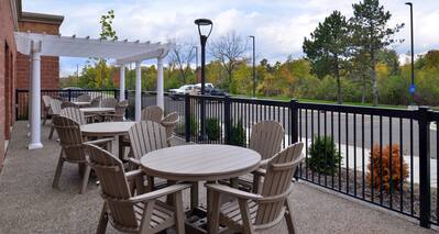 Daytime View of Hotel Patio With Tables, Chairs, Pavilion, and View of Guest Cars on Parking Lot