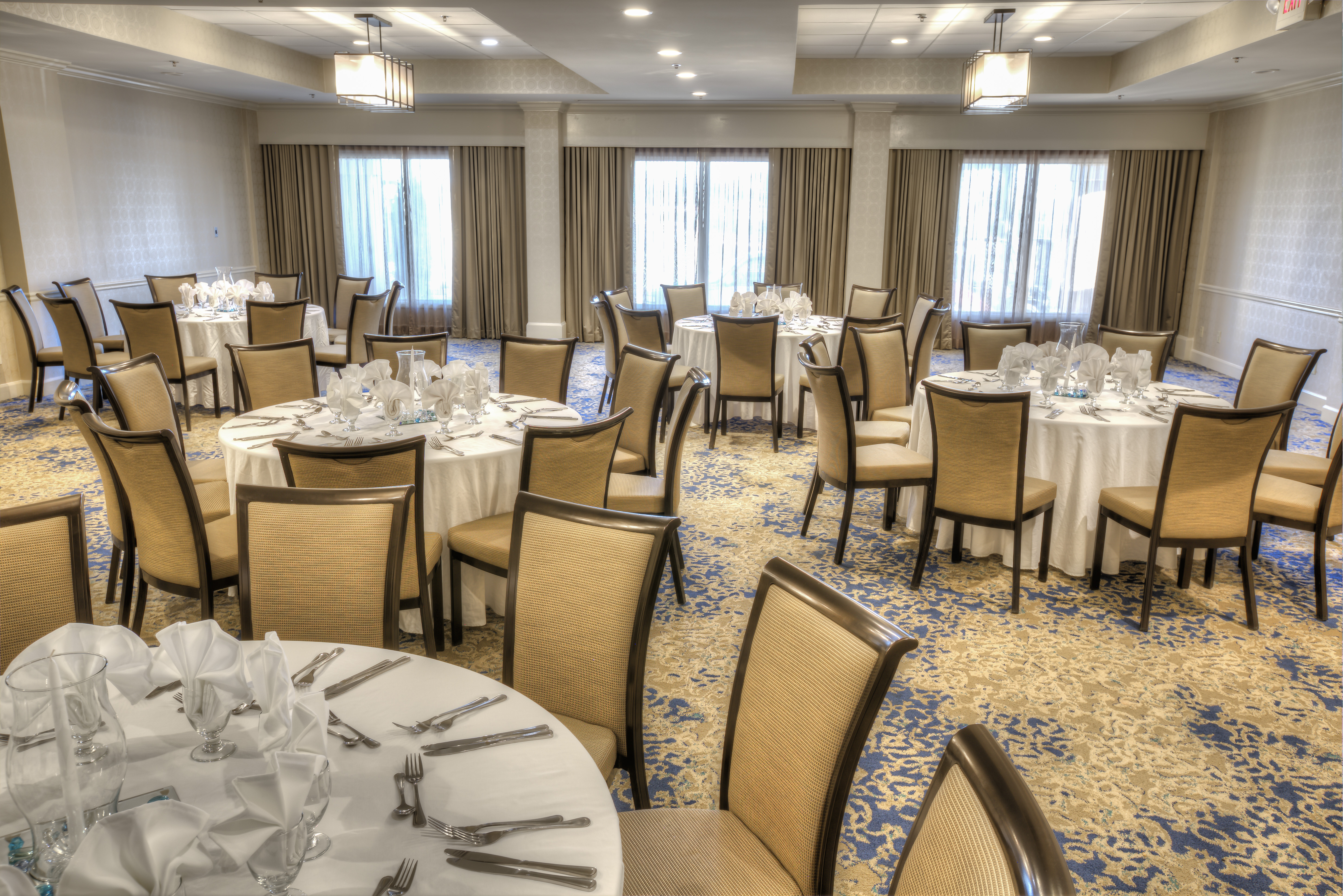 Place Settings on Round Tables With White Cloths and Windows in Event Space
