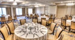 Overview of Place Settings on Round Tables With White Cloths and Windows in Meeting Space