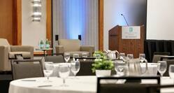 Spacious ballroom facility featuring impeccably set tables, interview style setup on stage, and podium.