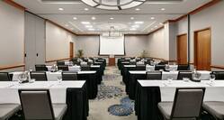Spacious meeting room facility equipped with classroom style tables, projector screen with equipment, and podium.