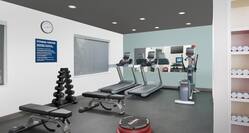 Fitness Center With Two Weight Benches, Free Weights, Cardio Equipment Facing a Large Mirror, Aerobic Step, and Towel Station