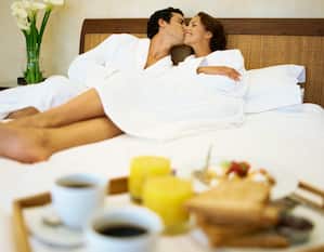 Tray of Breakfast Foods and Couple Wearing White Robes in Bed