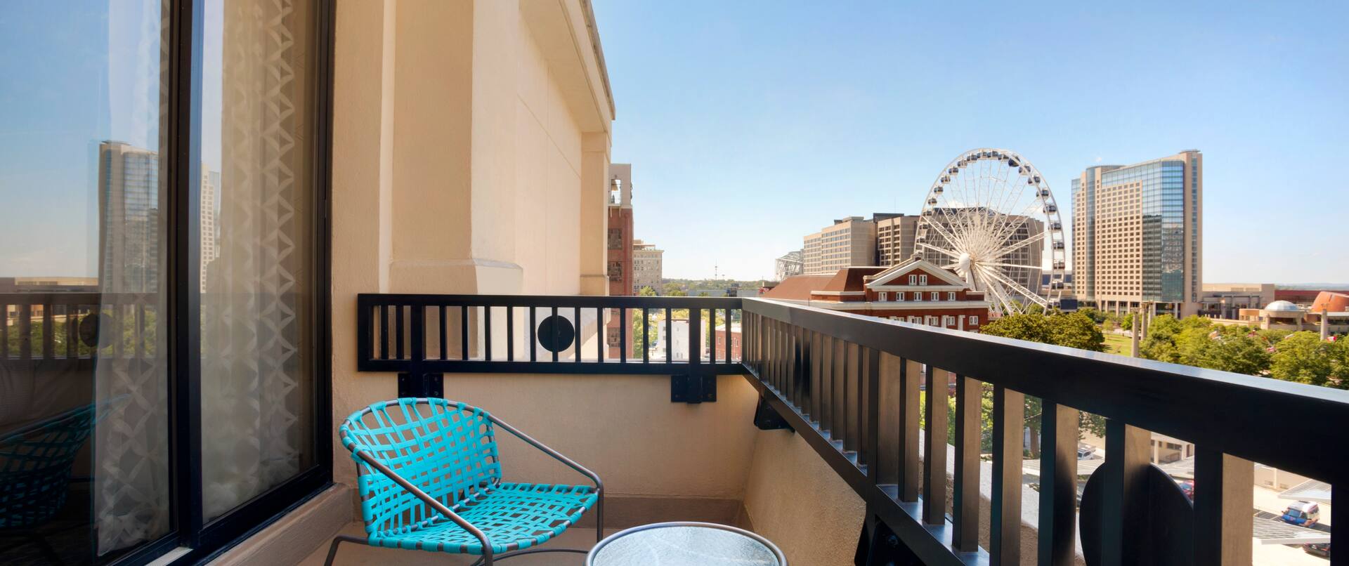 Two Teal Chairs and Table on Guest Room Balcony With View of SkyView Ferris Wheel on a Sunny Day