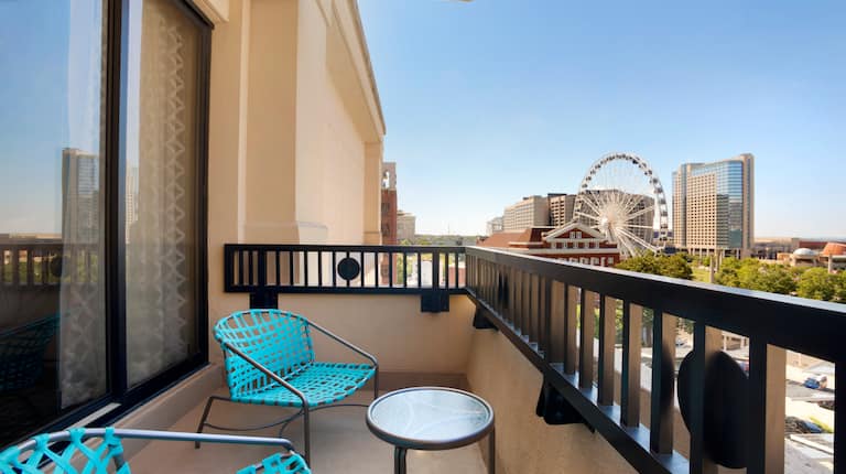 Deux chaises bleu sarcelle et une table sur le balcon d'une chambre donnant sur la grande roue SkyView par une journée ensoleillée