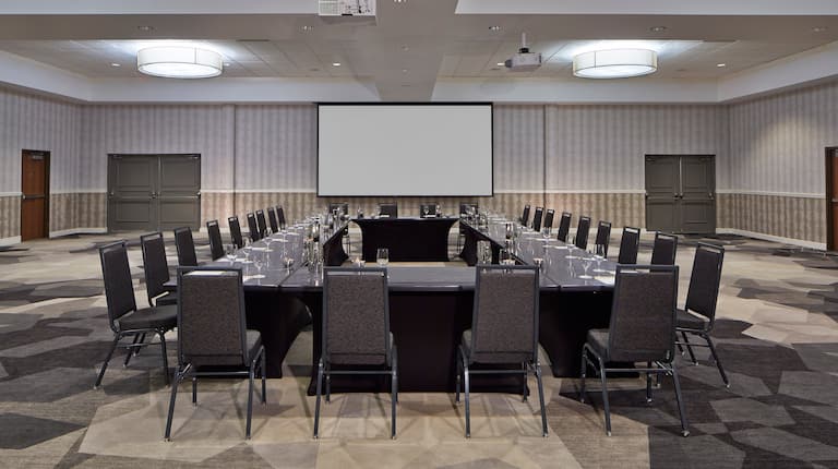 Meeting Room With Projector Above Hollow Square Table With Black Chairs and Projector Screen