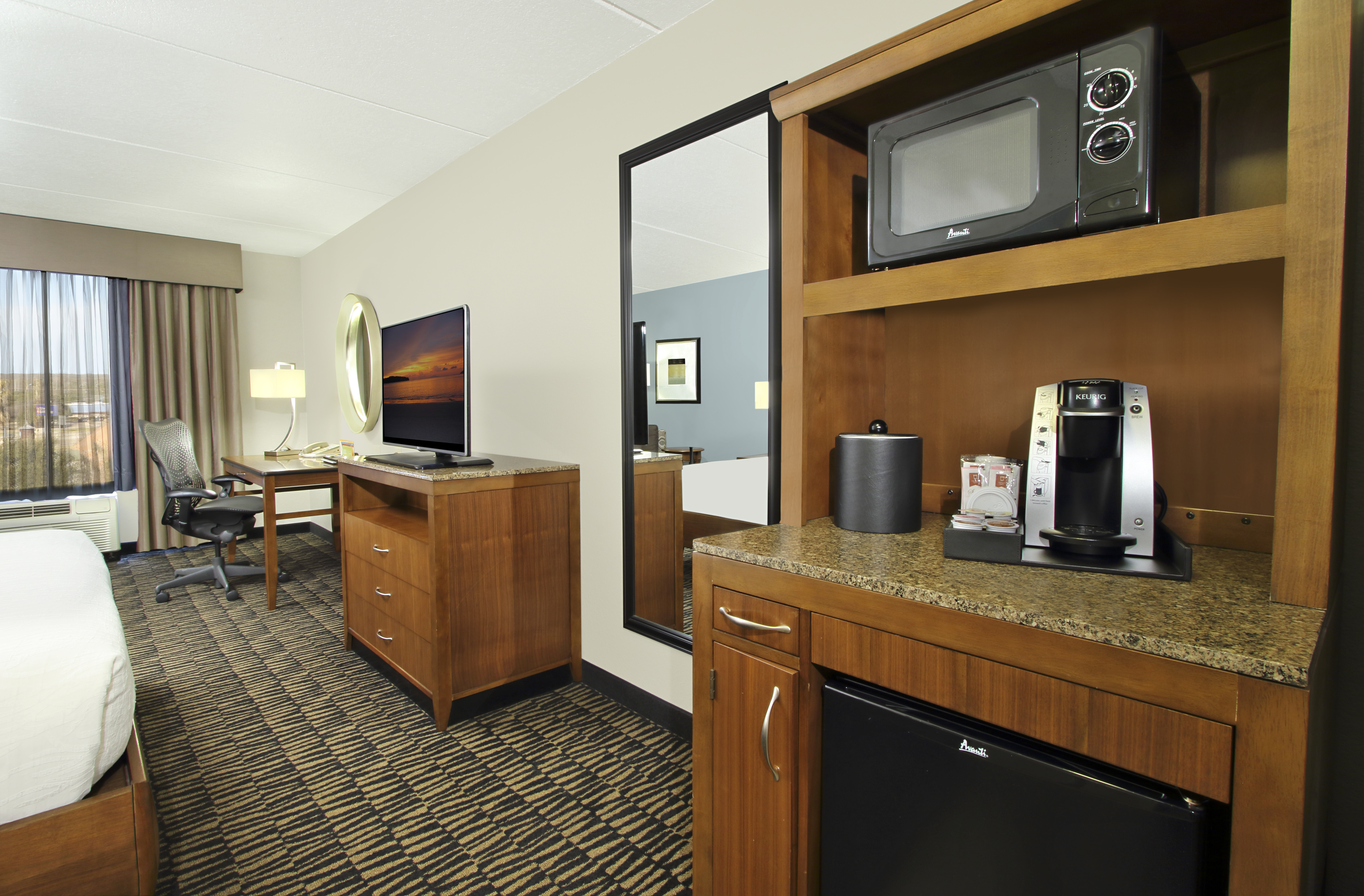 In-room hospitality center with microwave, coffee maker, and fridge with view of TV and work desk.