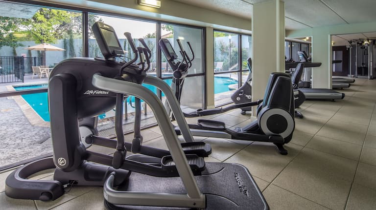 Fitness Center With Cardio Machines Facing Large Window With Pool View