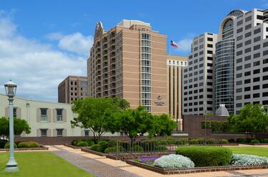 Daytime View of Hotel Exterior, Signage, Flagpole, and Landscaping From Grounds of Texas State Capitol 