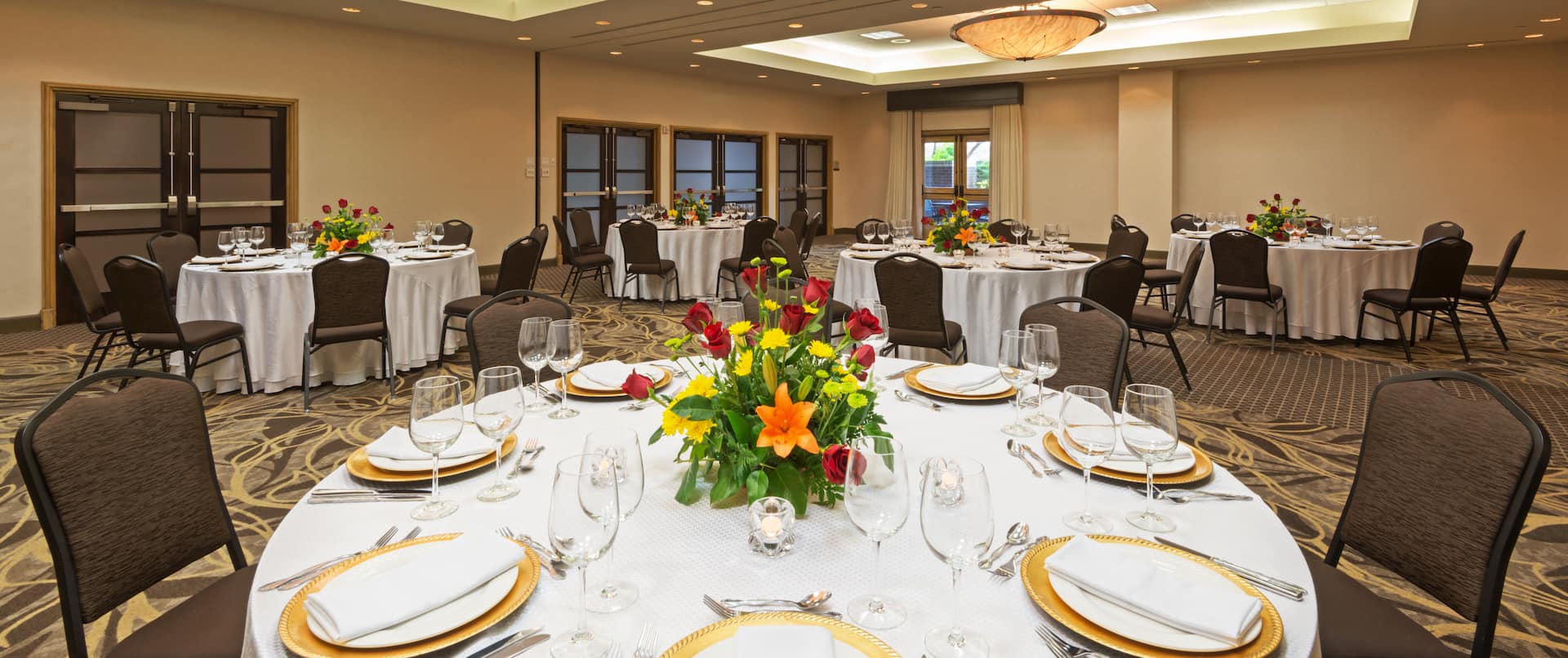 Round Tables in Ballroom With Place Settings, Flowers and Candles on White Tablecloths