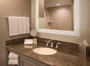 Detailed View of Showerhead Reflected in Brightly Lit Vanity Mirror, Sink, Fresh Towels, and Amenities in Standard Bathroom