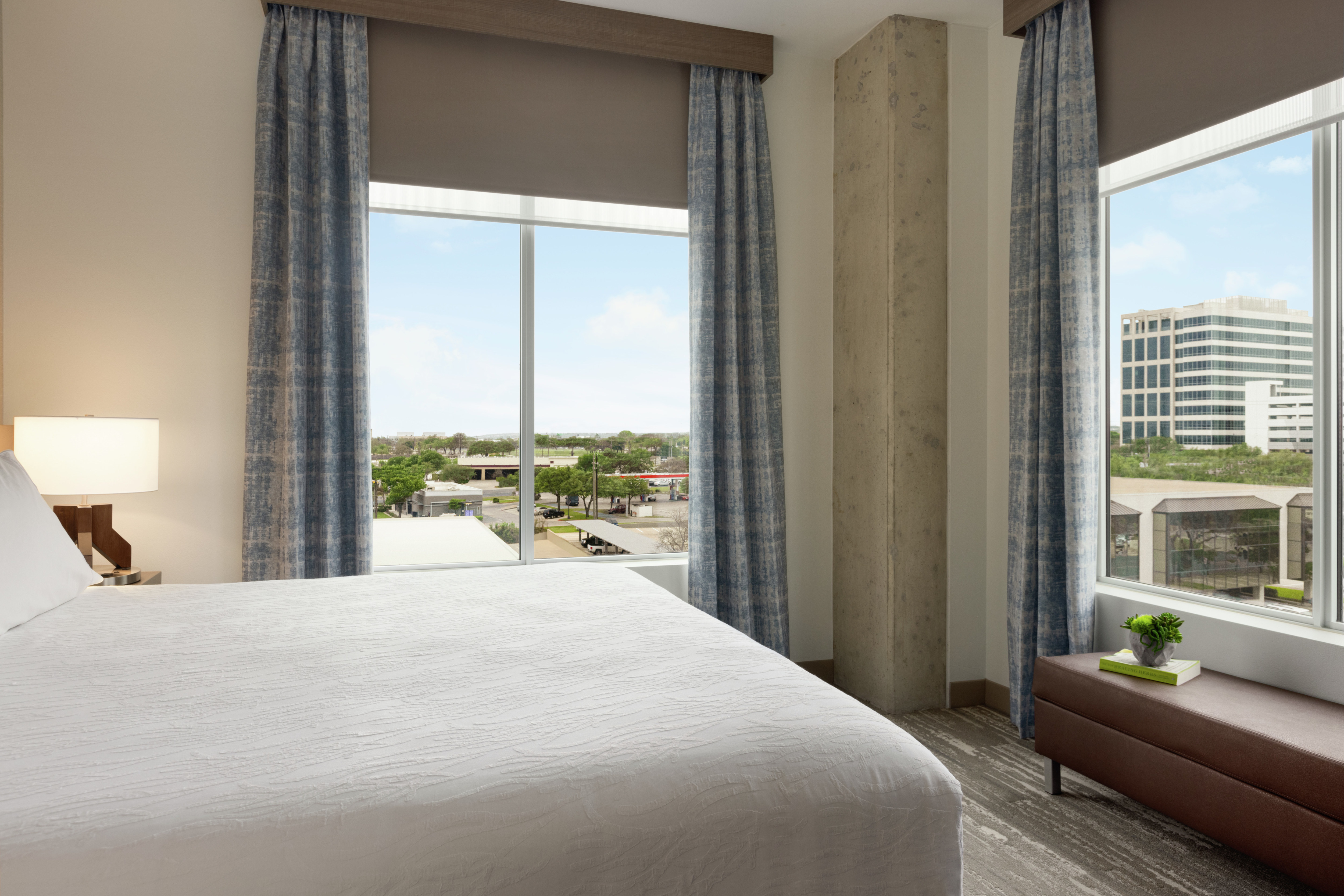 Bright private bedroom in suite featuring comfortable king bed and corner windows with stunning  downtown view.