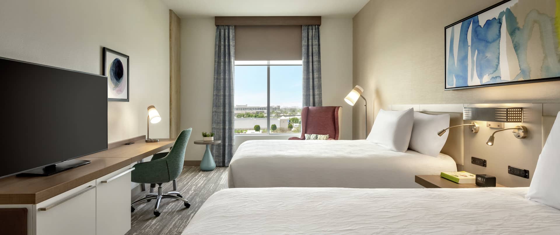 Spacious guest room featuring two comfortable queen beds, TV, work desk, and beautiful outside view.