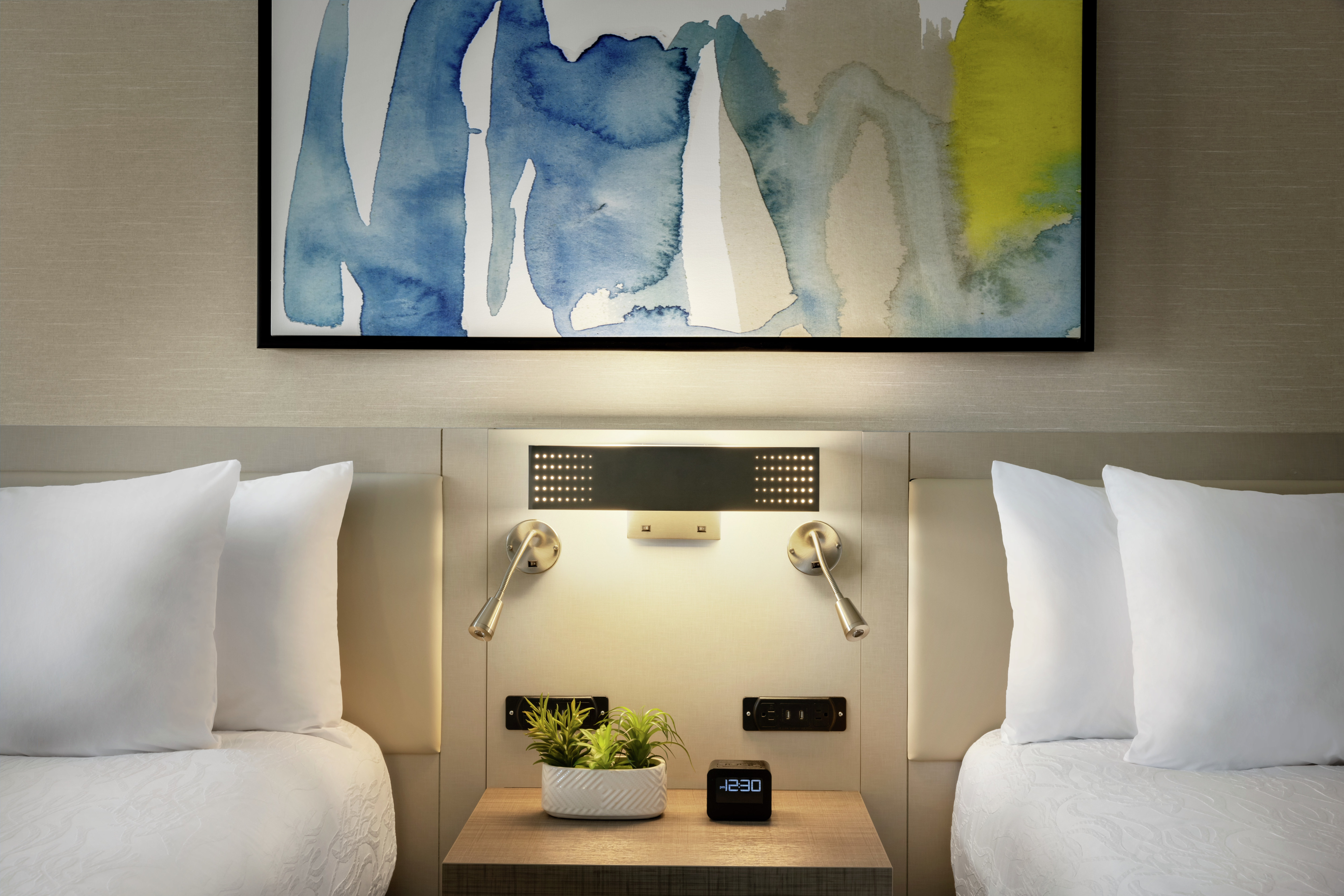 Stylish guest room featuring two comfortable queen beds, side table, and abstract art. 