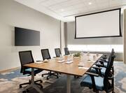 Bright meeting room featuring boardroom table, TV, and projector screen.