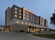 Front view of modern Hilton Garden Inn hotel featuring flowing guest room lights and clear dusk sky.