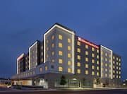 Modern Hilton Garden Inn hotel exterior featuring glowing guest room windows, pristine landscaping, and clear dusk sky.