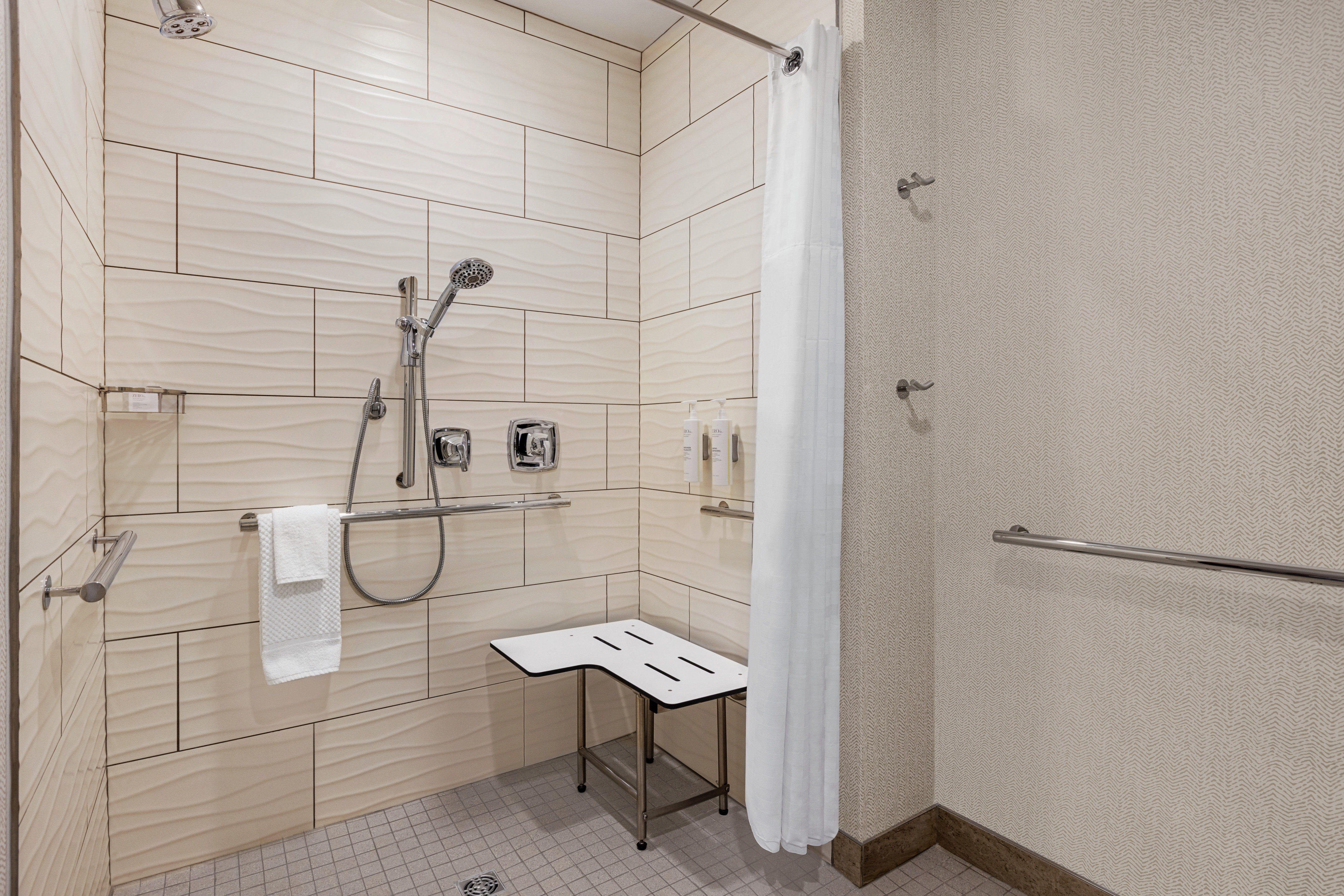 Spacious accessible bathroom featuring convenient roll-in shower with seat and grab bars for safety.