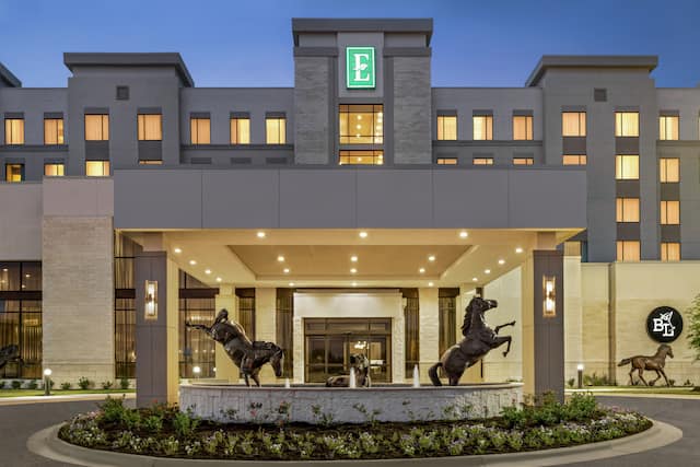 Modern Embassy Suites hotel exterior featuring porte cochere, stunning horse statues, and glowing guestroom windows.