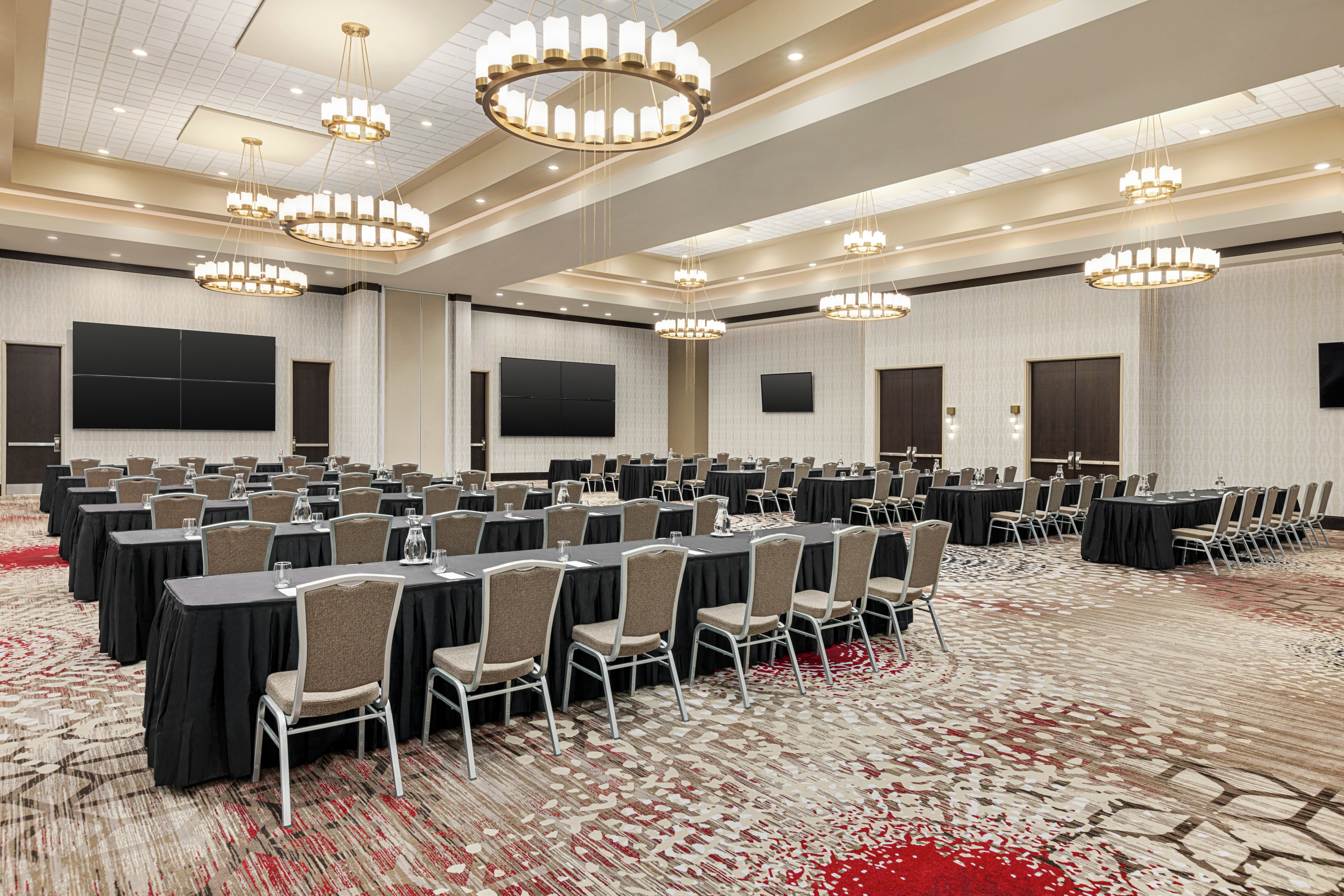 Spacious meeting room featuring a classroom style setup with ample seating and large TVs at front of room.