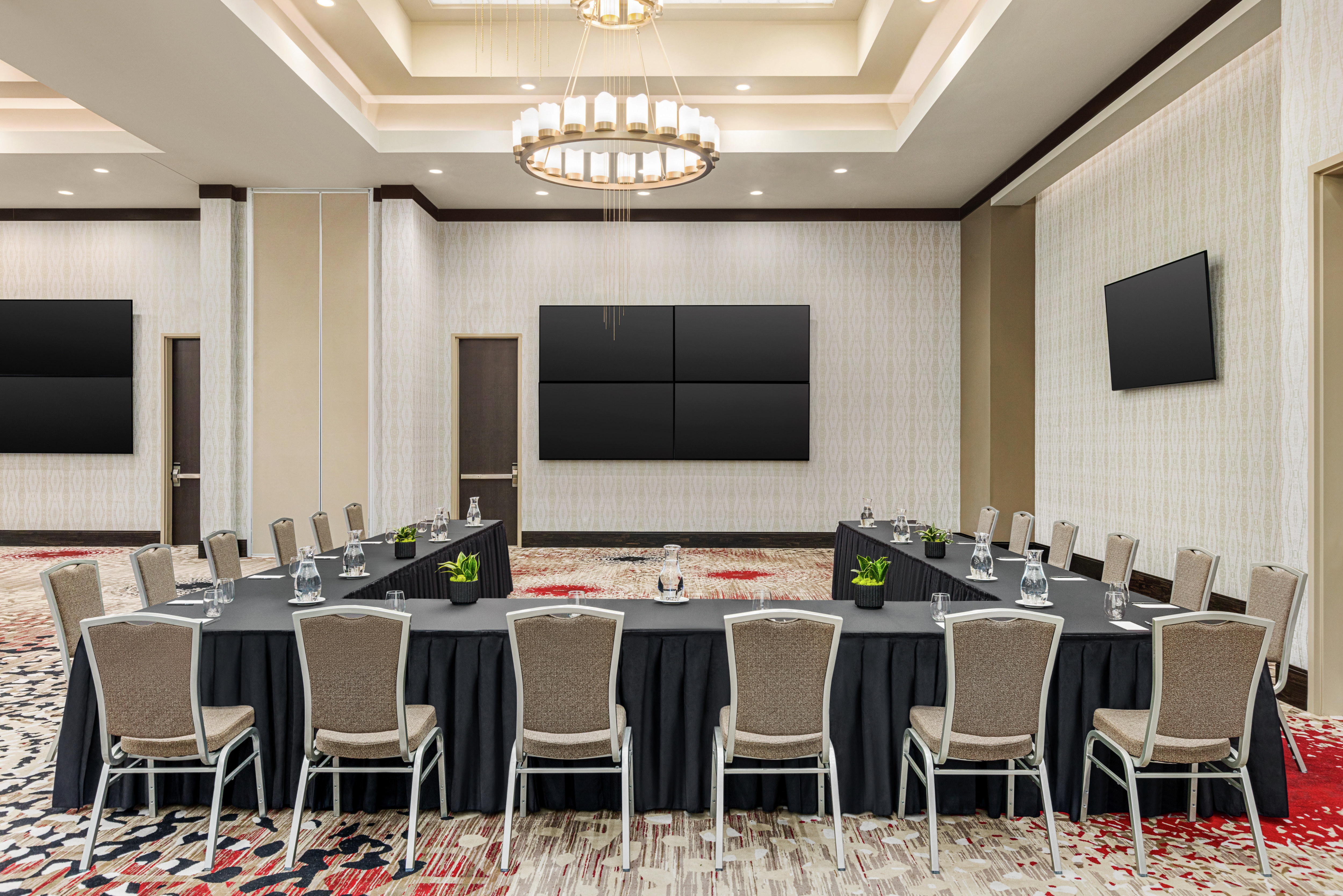 Spacious meeting room featuring u shape style setup, stylish design, and TV screens at front of room.