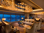 Illuminated Presidential Suite With Tables, Soft Seating, and Large Window With Lake View at Night