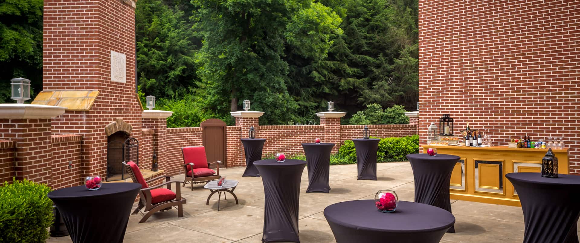 Round Tables With Black Table Covers, Beverage Station, and Red Lounge Chairs Set Up For a Reception on Burghley Terrace