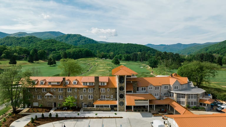 Birds eye view of golf club building with the course behind it and the mountains as the backdrop.