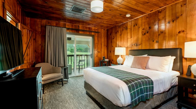 Room completely paneled with natural wood, one queen bed, and a glass door with views of golf course and mountains.