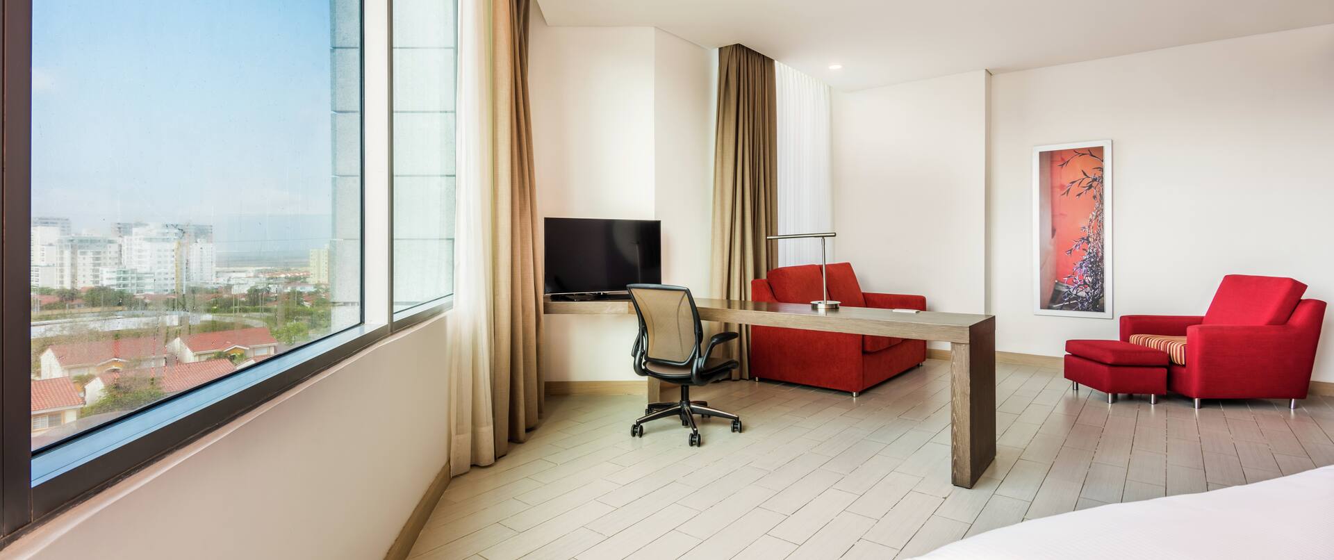 Spacious suite with expansive windows, desk with chair, armchairs and HDTV.