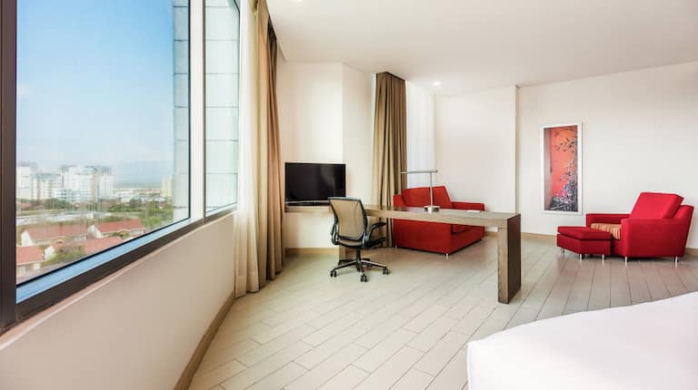 Spacious suite with expansive windows, desk with chair, armchairs and HDTV.