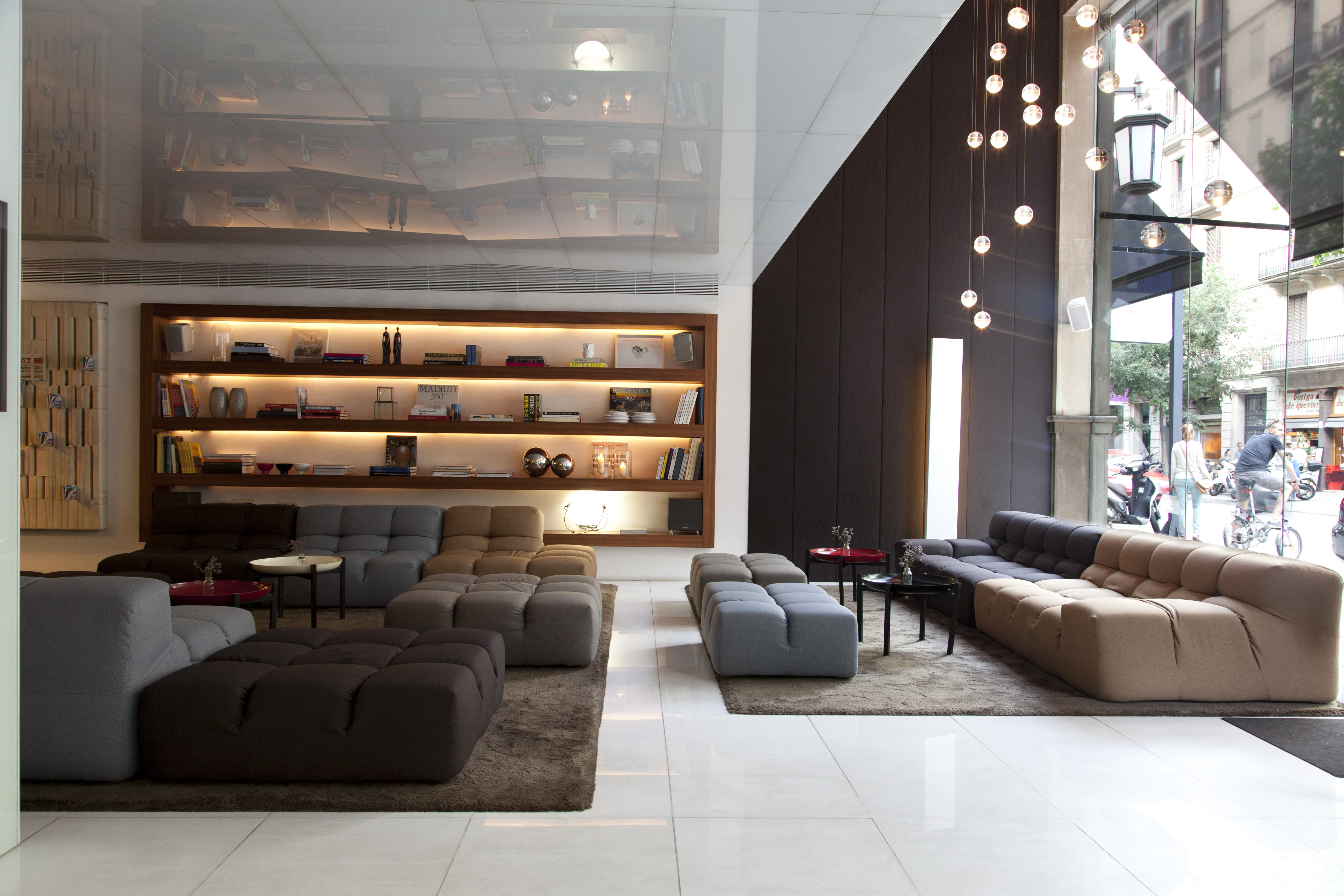 Lobby With Illuminated Shelves, Soft Seating and Decorative Lighting in Lobby Lounge Area by Large Window With View of People on the Street